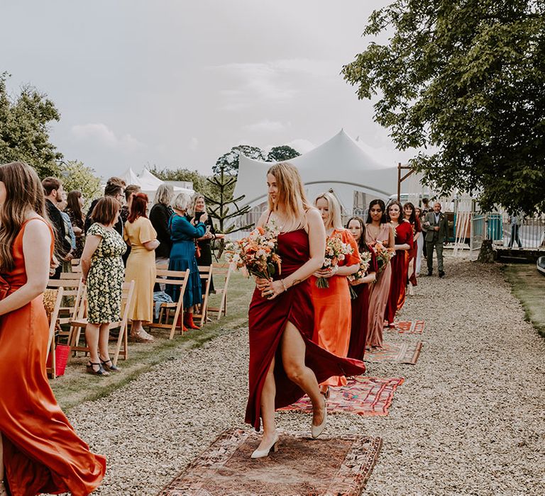 Bridesmads in Autumnal colour bridesmaid dresses walk down the aisle during outdoor wedding ceremony 