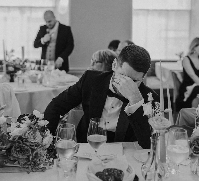 Groom in dark tux getting emotional listening to wedding speeches