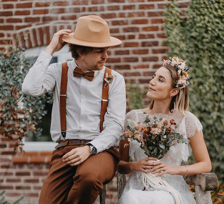 Bride in sheer eyelash lace boho wedding dress sitting with the groom in a striped shirt and brown hat for their rustic wedding 