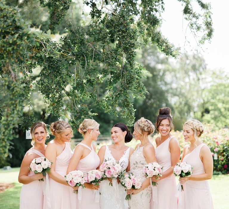 The bride smiles with her bridesmaids in pale pink dresses in a variety of styles and silhouettes 