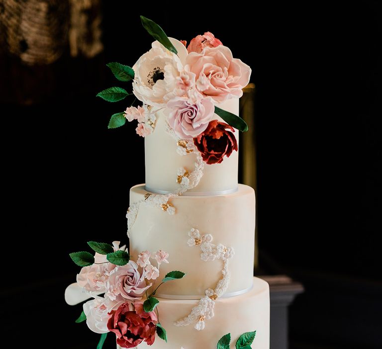 Three tier white frosted wedding cake complete with fondant floral decor and gold sugar balls 