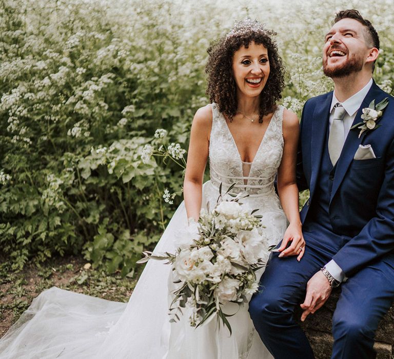 Bride wears lace wedding dress with boho style and sits beside her groom in three piece suit 