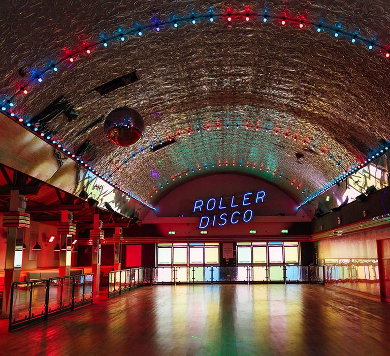 Large roller disco hall at Margate Dreamland with colourful windows, a large disco ball and colourful fairy lights 