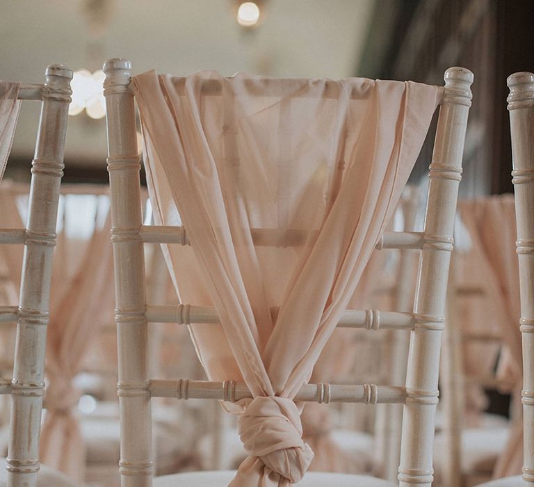 White wooden wedding chairs for the wedding ceremony decorated with pink sashes tied in a knot 