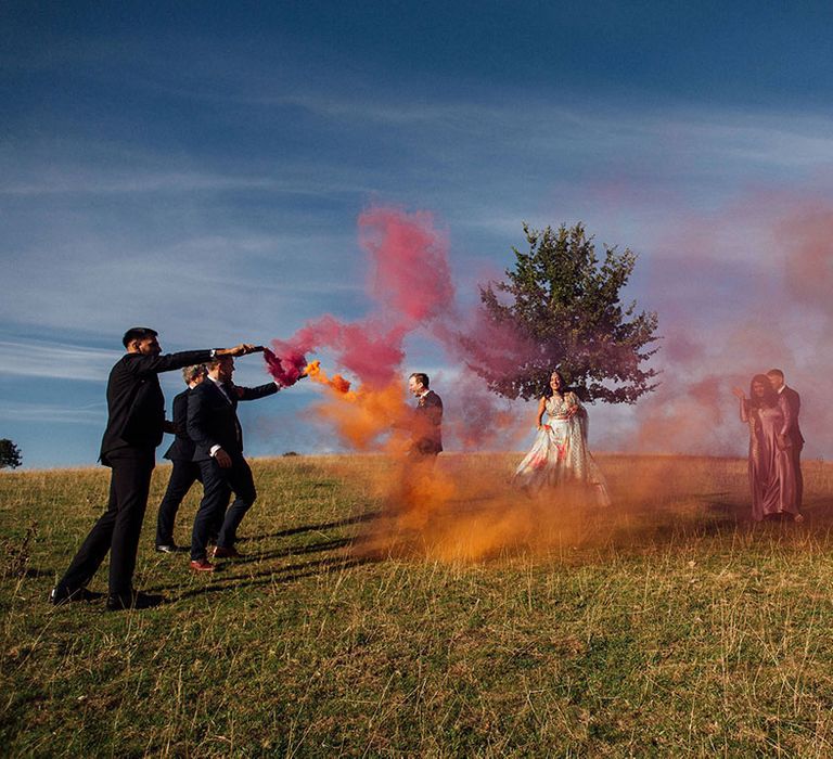 Bride & groom stand with their wedding party during colourful smoke bomb portraits 