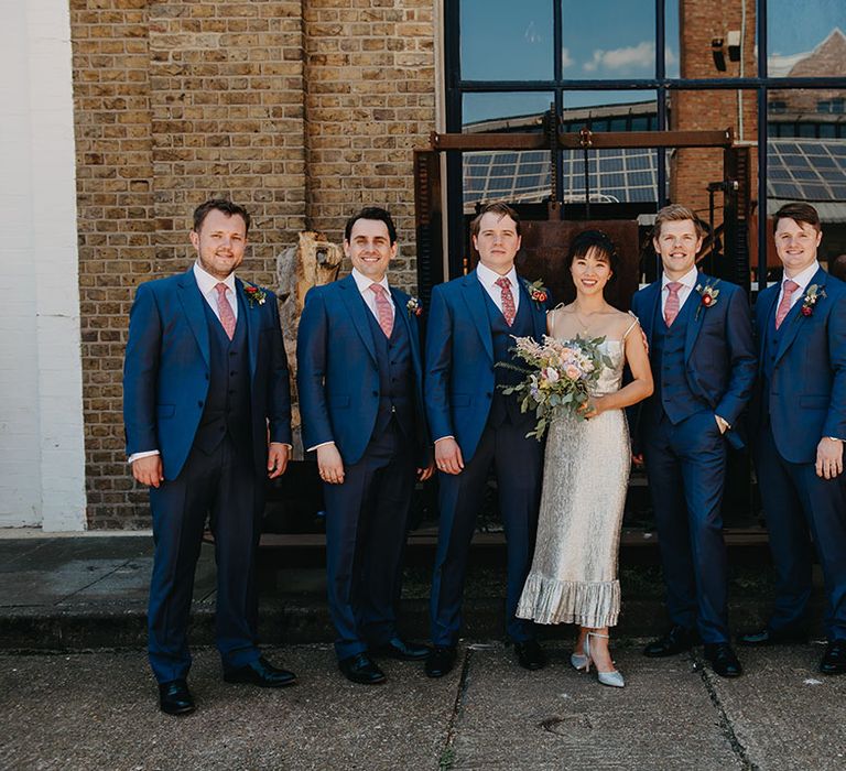 Bride stands with groomsmen in three piece blue suits at Trinity Buoy Wharf