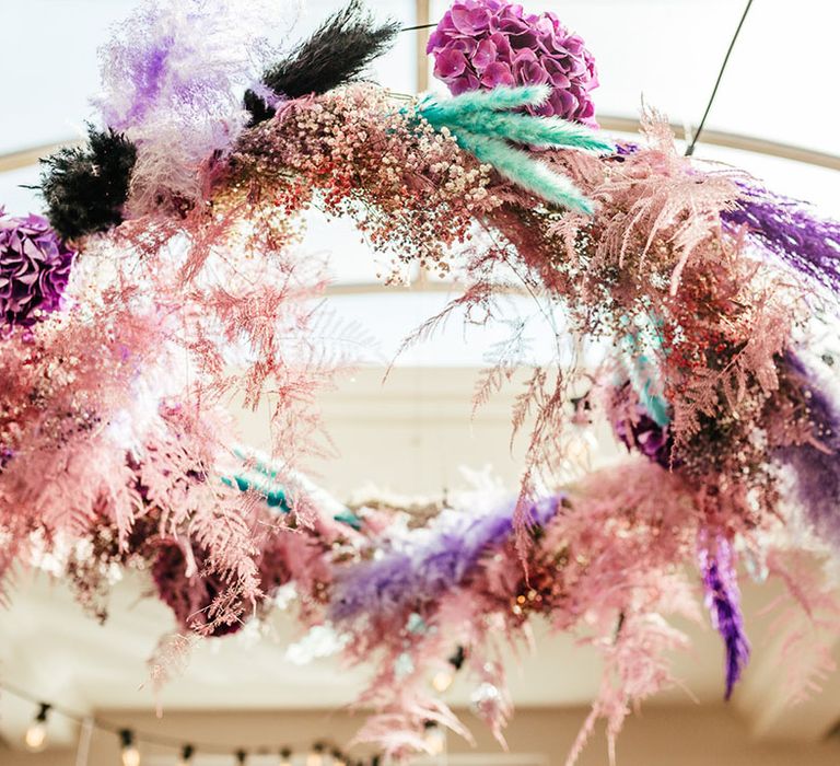 Suspended baby pink, teal, white and black pampas grass wedding decor with purple carnations and dried flowers 