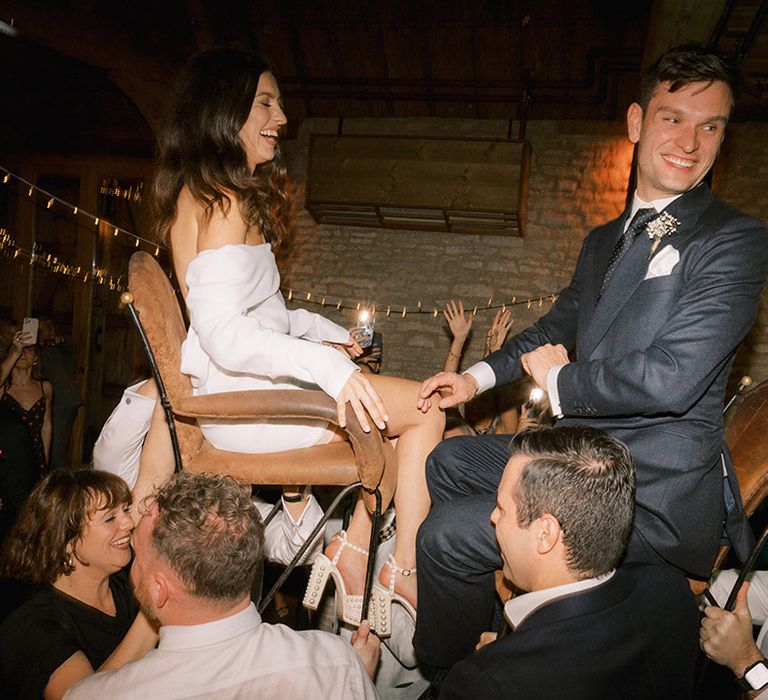 The bride and groom sit on chairs and are lifted up by their wedding guests for a Jewish wedding tradition  