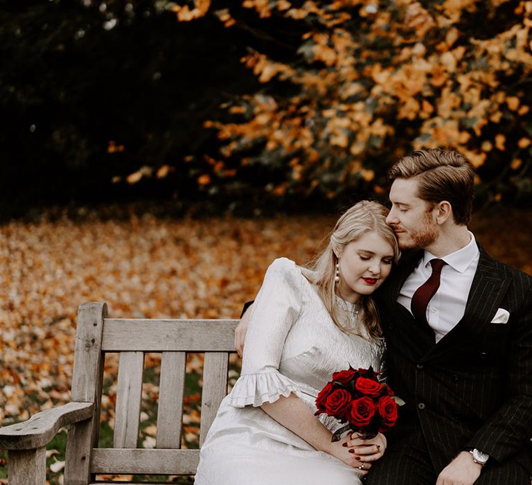 Bride in sparkly wedding dress with shoulder pads and ruffle sleeves holding red rose bouquet with the groom in pinstriped suit 