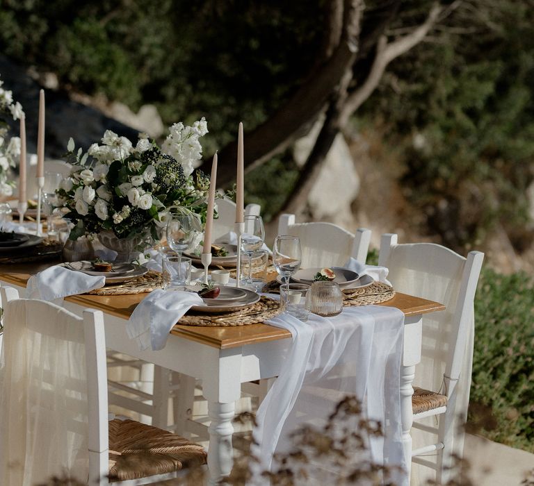 Greek wedding tablescape featuring blush tapered candles, figs, ribbed jars, wine glasses and floral decor that includes white berries, italian ranunculus and eucalyptus