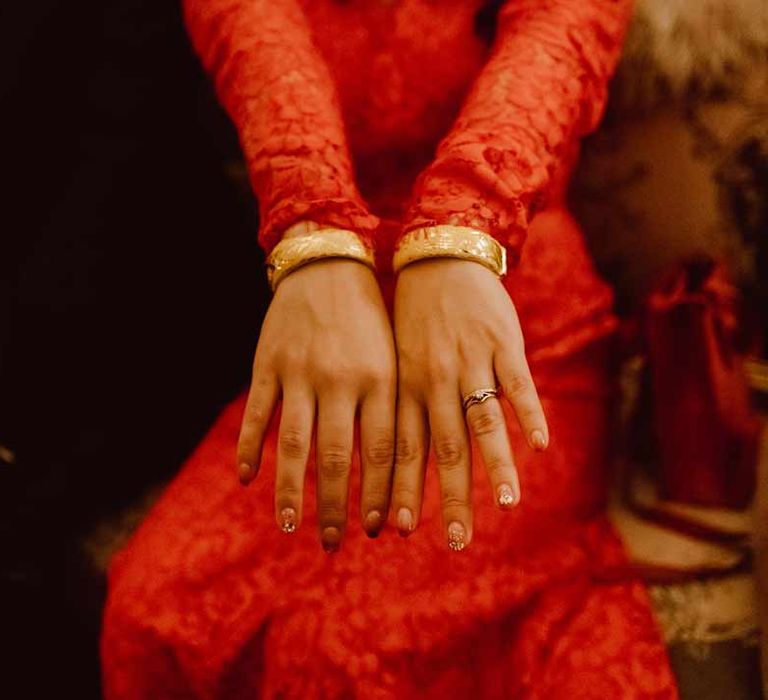 Bride in red lace wedding dress with long sleeves showing gold wedding bangles, gold wedding ring and gold wedding nails 