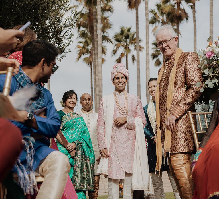 Groom waiting at the end of the aisle light pink sherwani, light pink shoes and light pink turban and cream trousers  