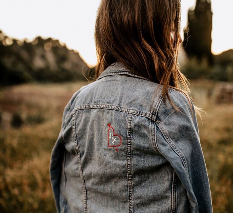 Bride in a classic blue denim jacket with a small embroidered arrow going through a heart with the bride and groom's initials 