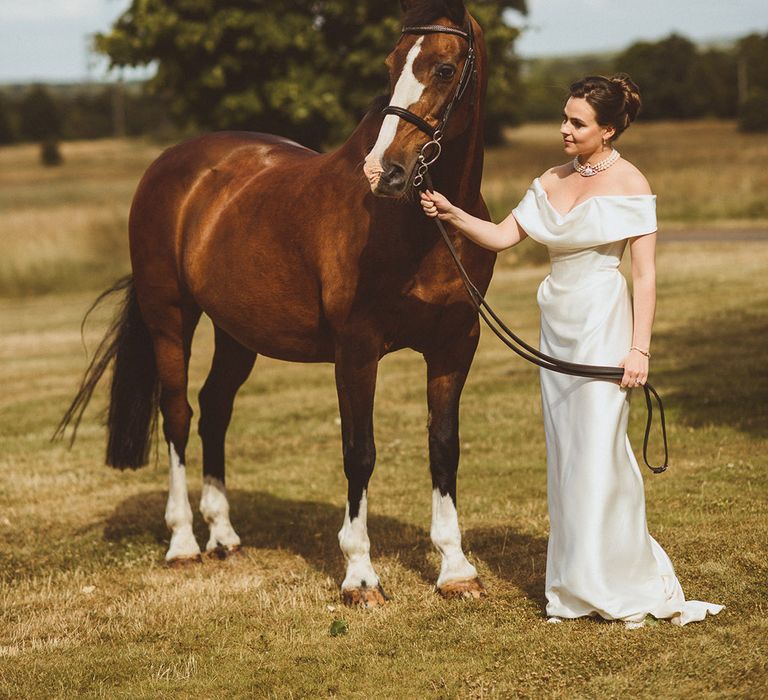 Bride in off the shoulder bridal gown with dark brow horse on the wedding day 