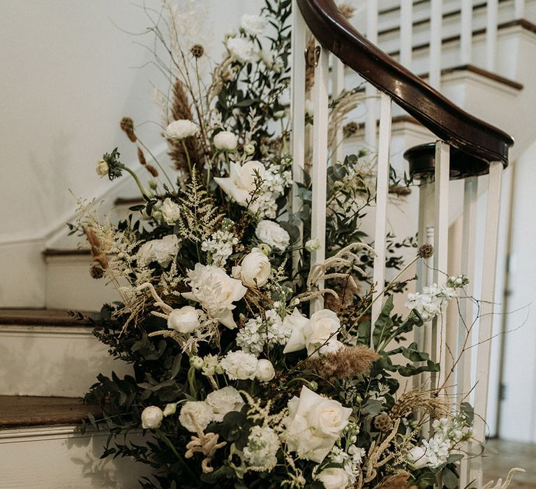 All white wedding flowers decorating the staircase at Aswarby Rectory with dried grass for natural style wedding 