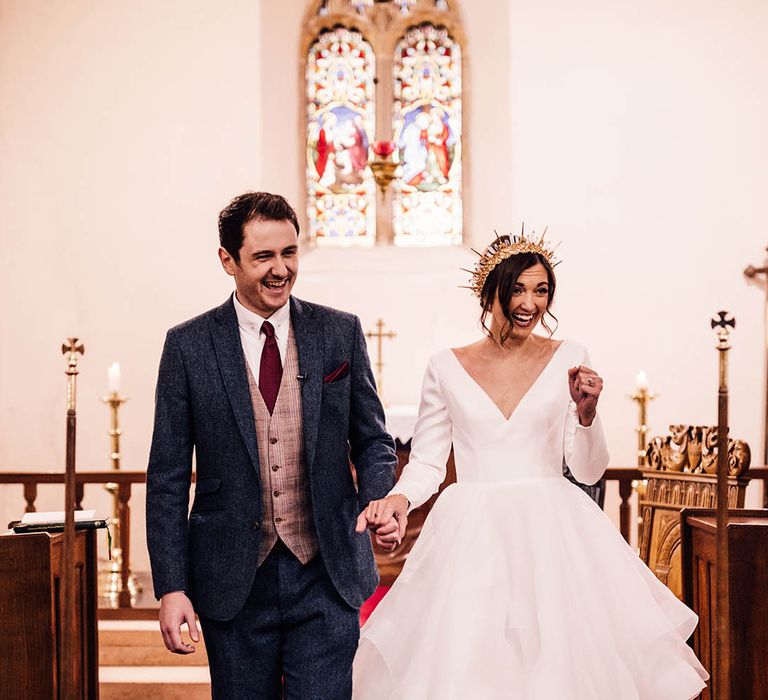 Groom in three piece navy suit walking back down the aisle of the church with the bride in ruffle wedding dress 