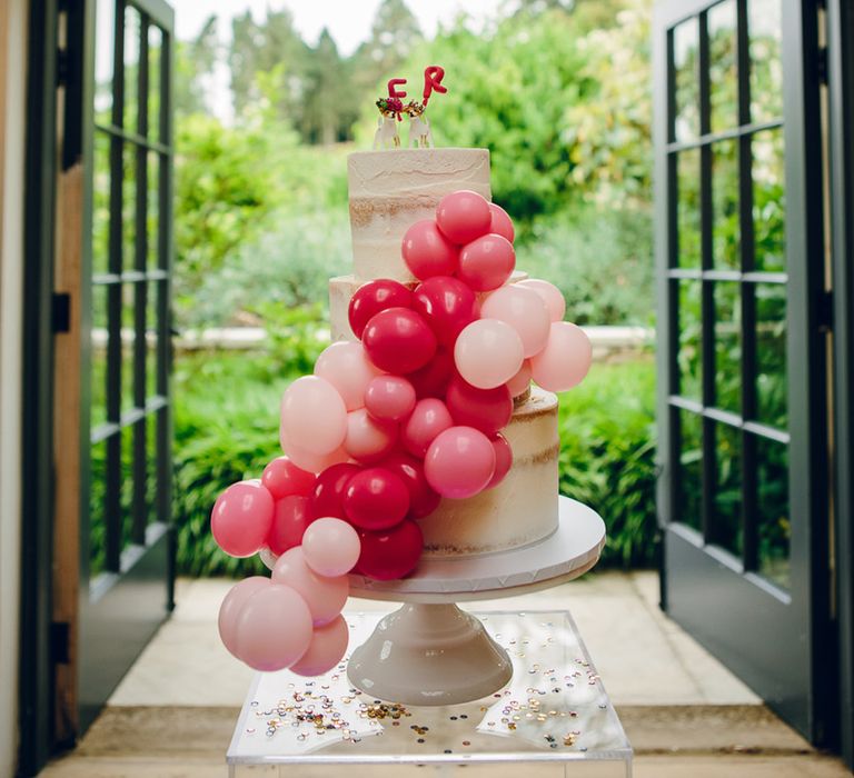 Three tier semi-naked wedding cakes decorated with pink balloon decorations and personalised cake topper 