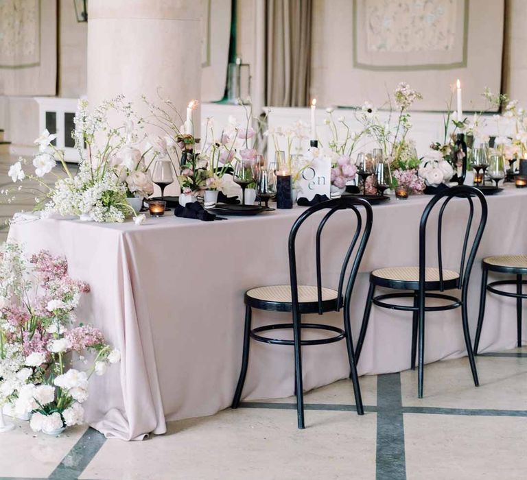 Notan inspired wedding tablescape consisting of light pink wedding tablecloth, white poppies, light pink Persian buttercups, baby's-breath and foliage centrepieces, black artistic candlestick holders, white tapered candles, black crockery and monochrome wedding stationery 