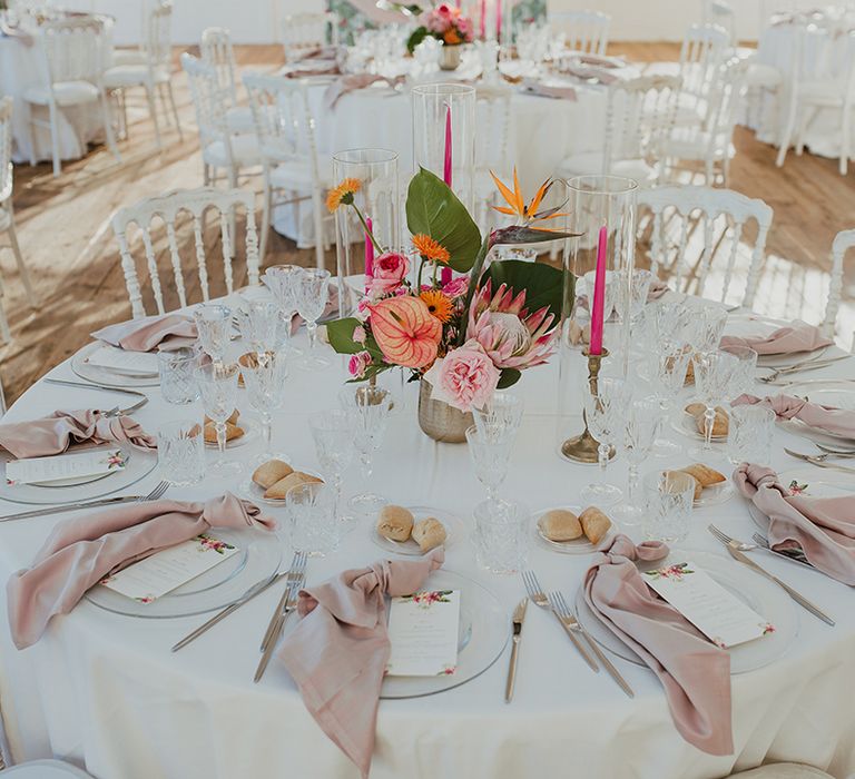 round wedding table at bride in strapless wedding dress and groom in a grey suit dancing up the aisle as husband and wife at their outdoor italian villa wedding reception with tropical flower centrepiece and light pink linen napkins