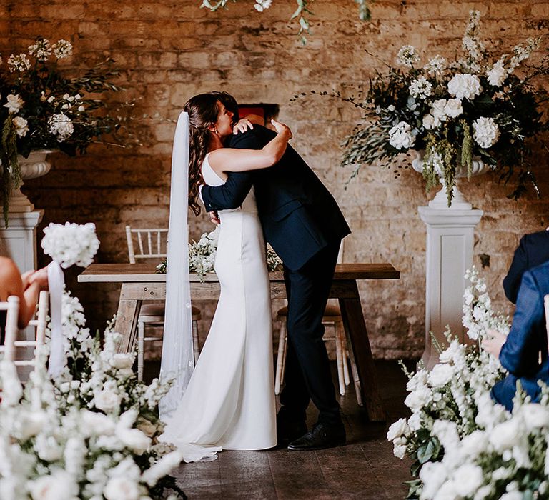 Bride in fitted wedding dress from Made With Love embracing groom at the altar 