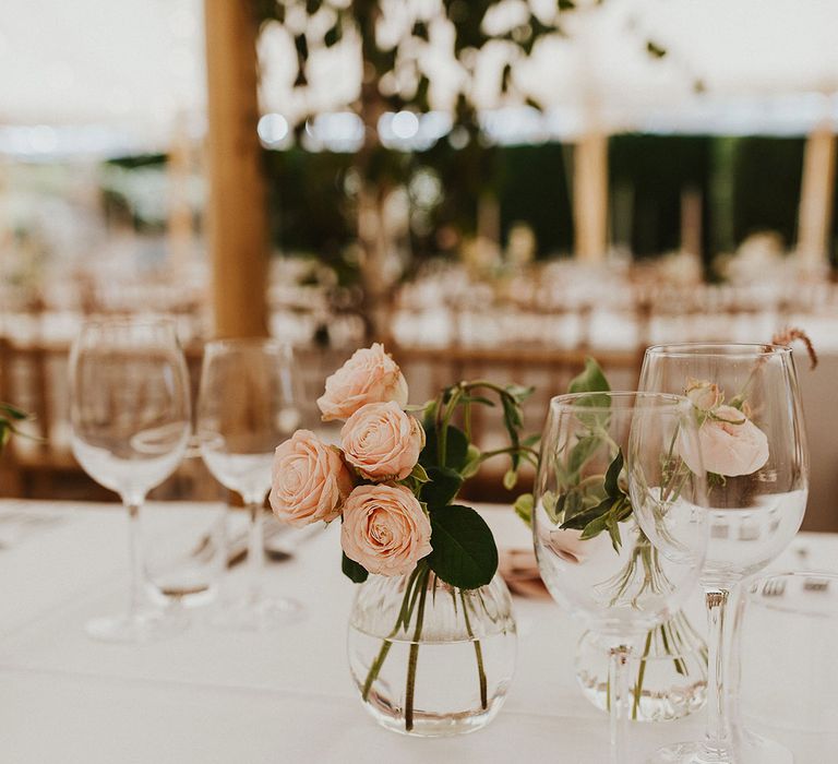 Marquee wedding breakfast with pale pink napkins, bud vases of white and pink roses and twinkling lights 