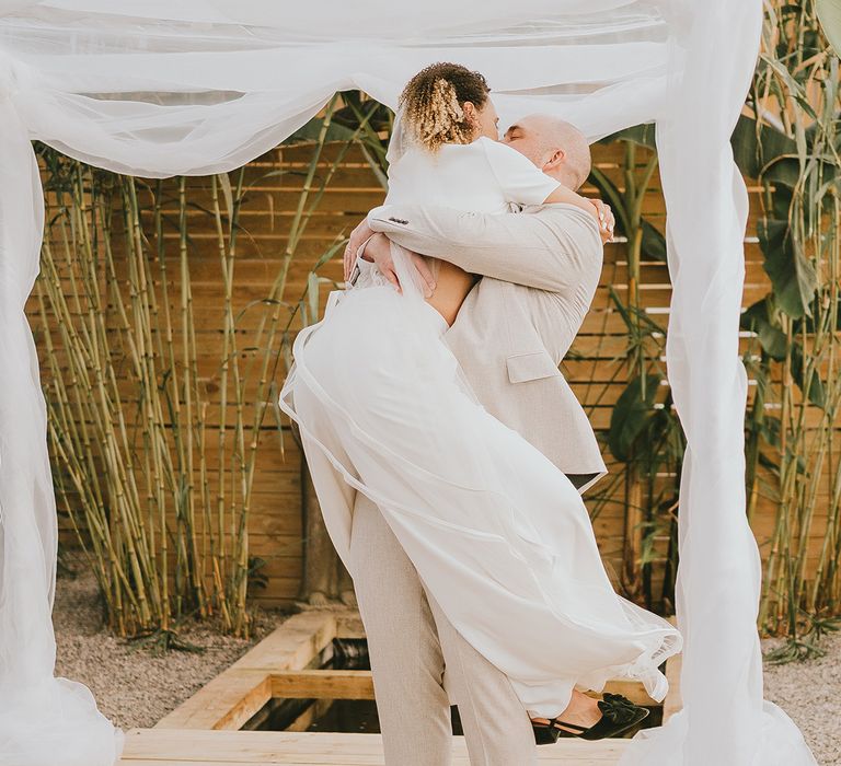 Bride wraps her legs around the groom as they share a hug at their wedding 