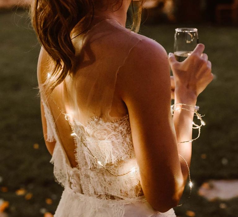 boho bride with high ponytail wedding hair style in a lace wedding dress and string lights