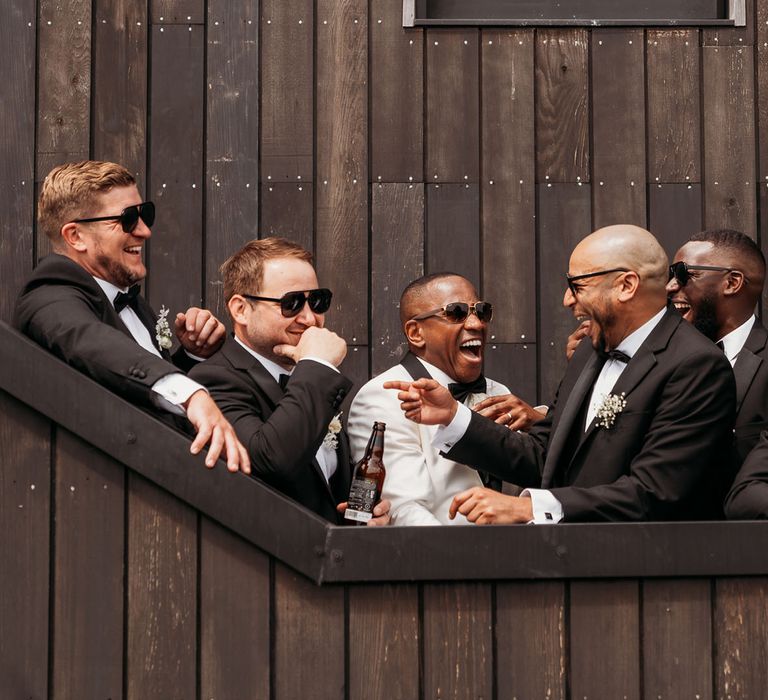 Groomsmen in-black tuxedos and sunglasses laughing on stairwell at Crumplebury wedding