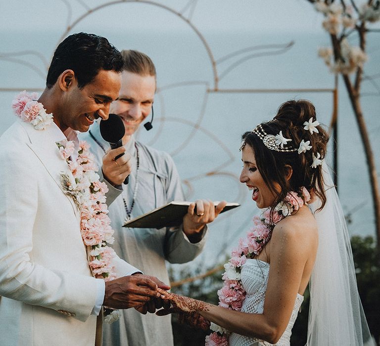 Bride in cream suit exchanges wedding bands with bride whilst wearing traditional pink flower Varmala