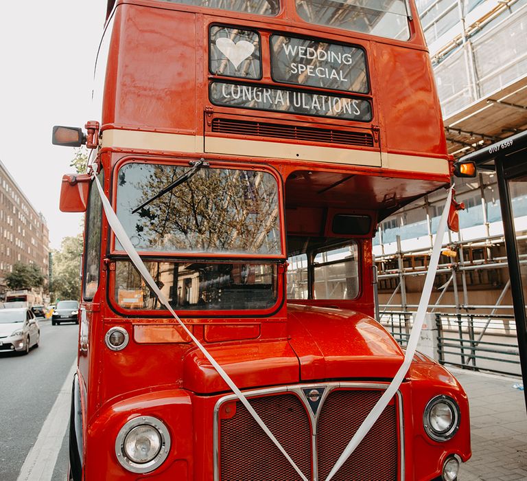 Red double decker bus wedding transport decorated with white ribbon 