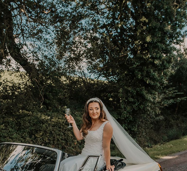 Bride in custom wedding dress posing in retro wedding car 