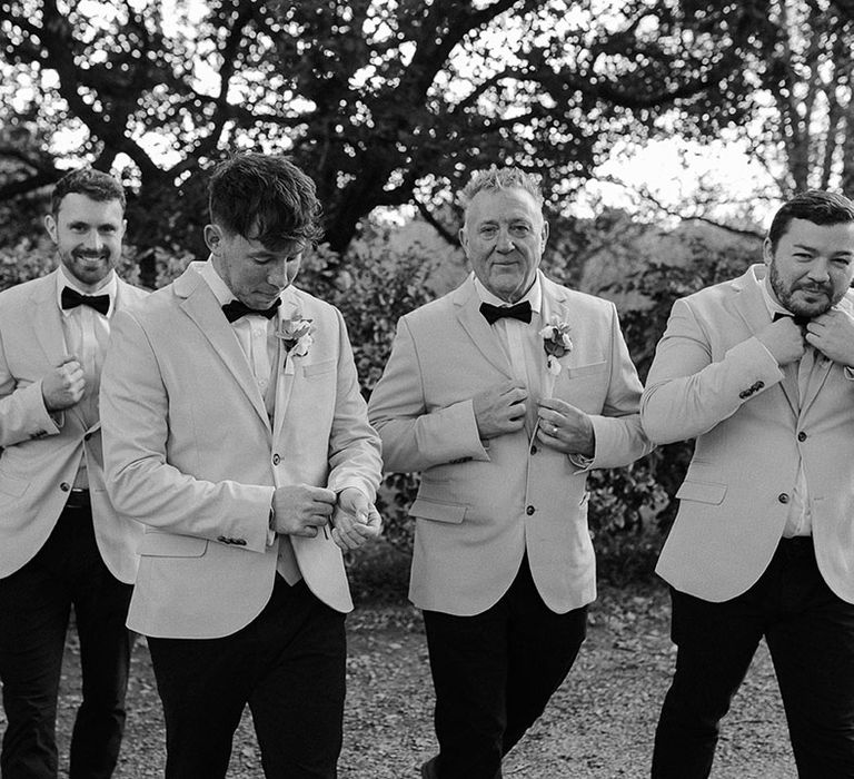 Black tie wedding fashion with the groom and groomsmen wearing matching beige suit jackets and black bow ties 