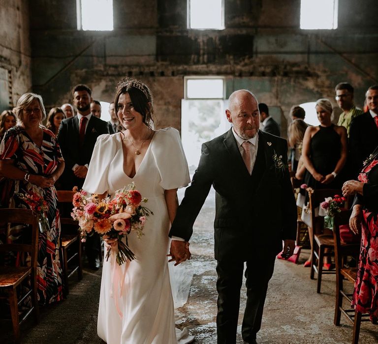 Father of the bride walks the bride down the aisle at wedding weight the brie wearing a puff sleeve wedding dress 