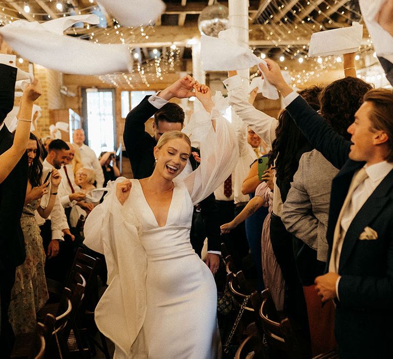 The bride and groom enter their wedding reception as the guests stand and wave napkins 