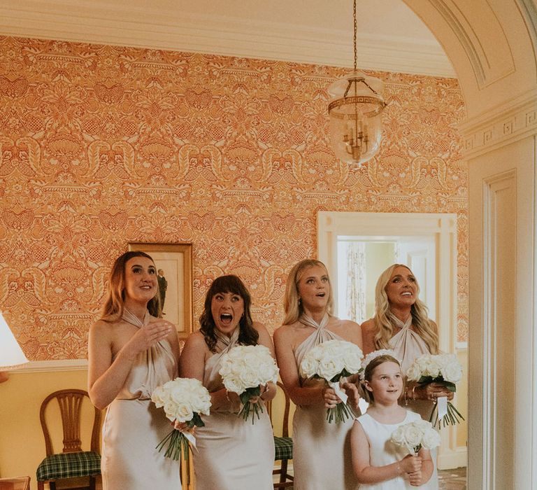 Bridesmaids in matching gold halterneck bridesmaid dresses get their first look at the bride 