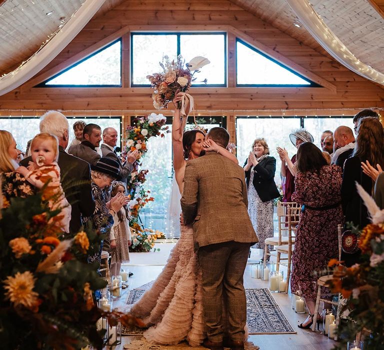 The bride and groom kiss as they walk back down the aisle together at the boho barn, Styal Lodge 