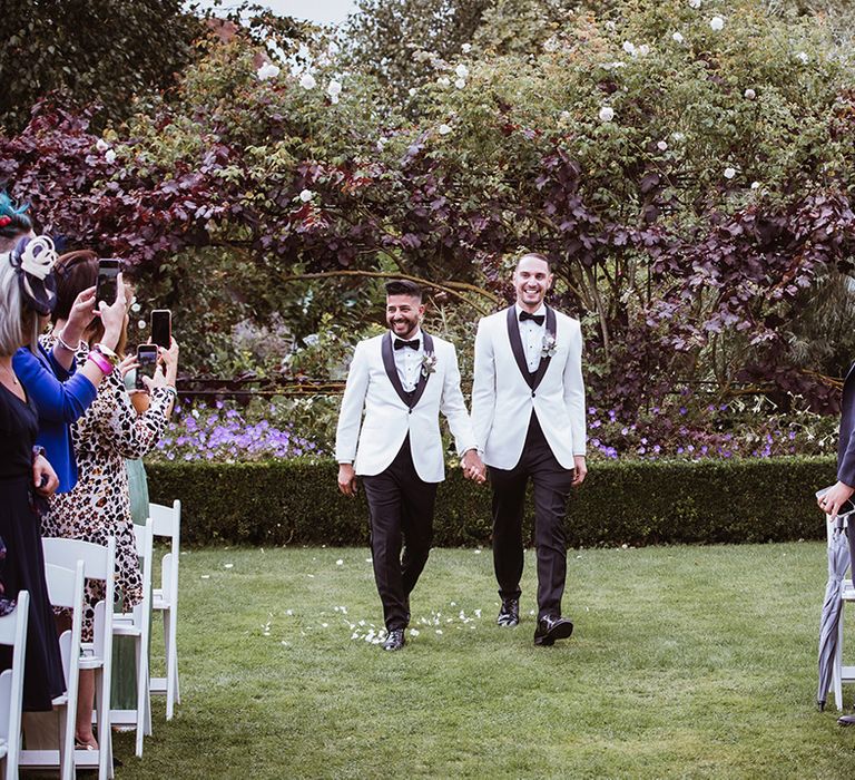 The grooms walk down the aisle together at country house outdoor wedding 