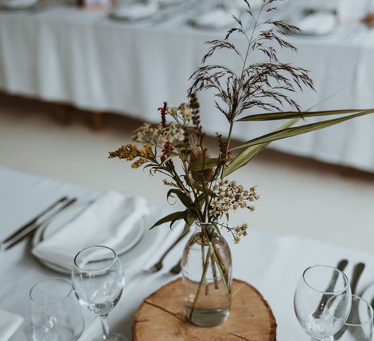 Rustic wood slice table centrepieces with minimalist flowers in glass vase 