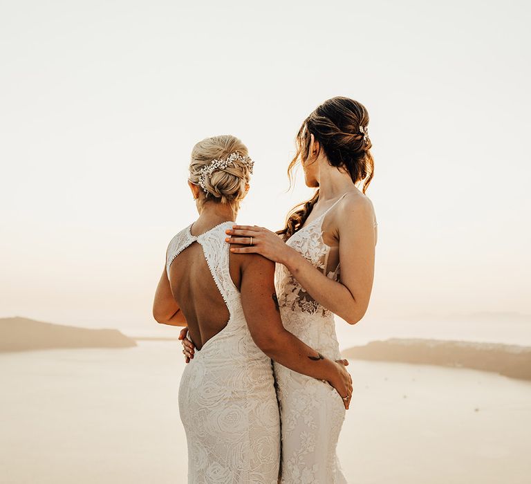 Two brides in lace wedding dresses with open back detail as the look out into the sunset at golden hour 