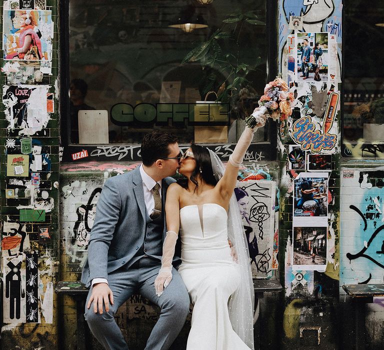 Bride in strapless wedding dress with pearl wedding veil and sheer gloves kissing groom at urban chic London wedding 