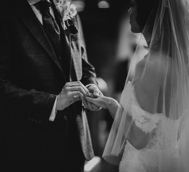 Black and white portrait of the groom putting on the brides wedding ring 