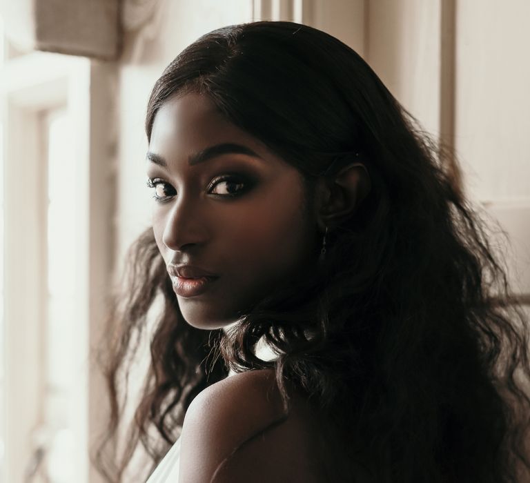 Hairstyles for Black brides. A Bride wears her hair in lose waves. She looks back over her shoulder to the camera showing off the waves.