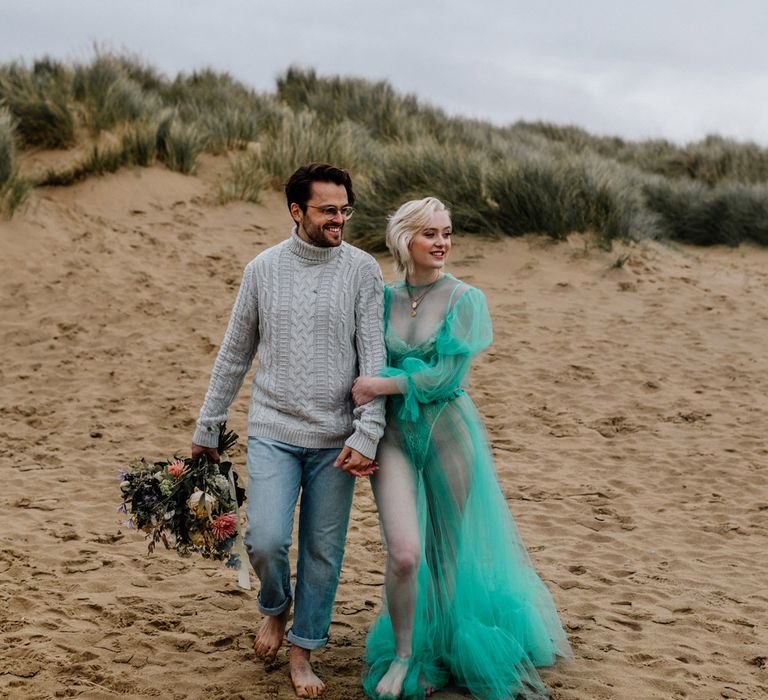 Stylish bride and groom walking barefoot in the sand at their intimate beach elopement 