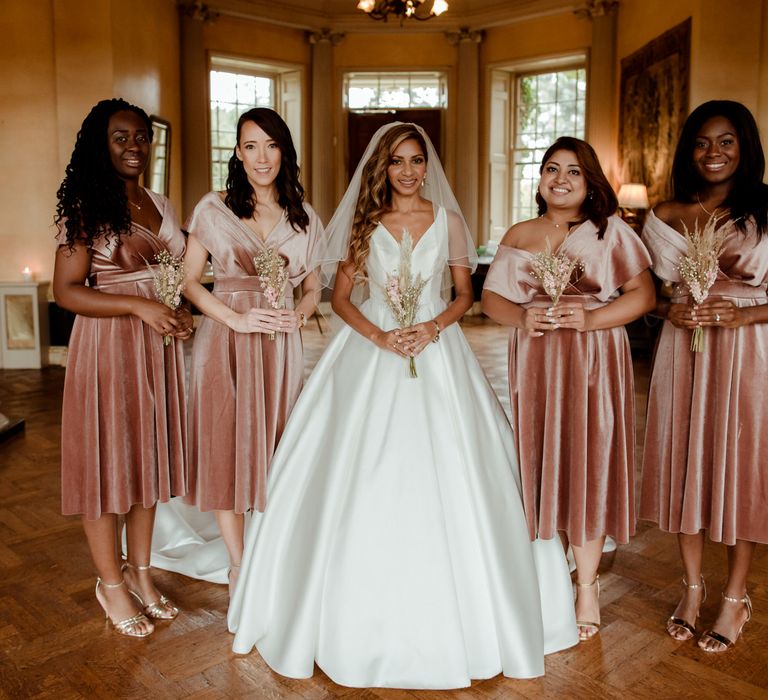 Bridal party portrait with bridesmaids in pink velvet dresses holding dried flower bouquets 