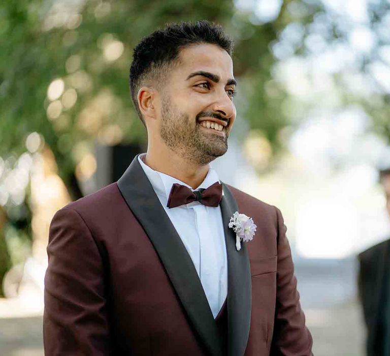 Groom in maroon suit with bowtie as he wait for his bride