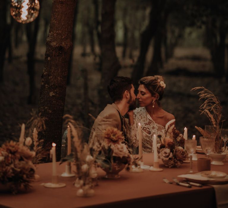 Boho bride and groom kissing at their intimate outdoor reception decorated with dried and fresh flowers and edison bulb lighting 