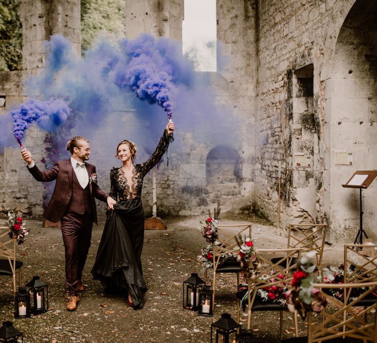 Bride and groom holding purple smoke bombs in an open air medieval abbey