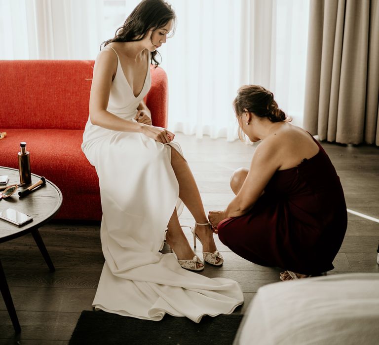 Bridesmaid putting on the brides peep toe wedding shoes with pearl detail 