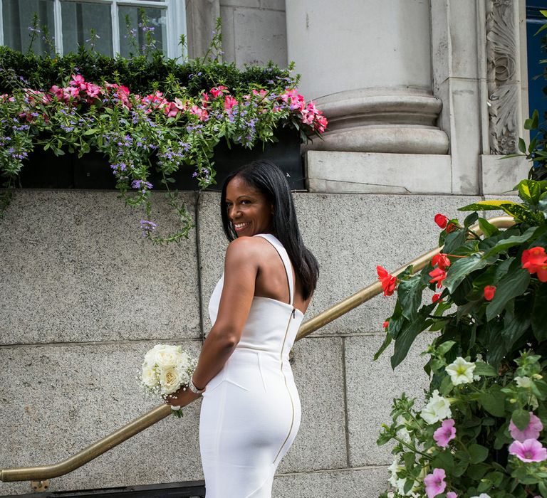 Beautiful bride in a fitted Roland Mouret dress with one shoulder detail holding a white rose and gypsophila bouquet 