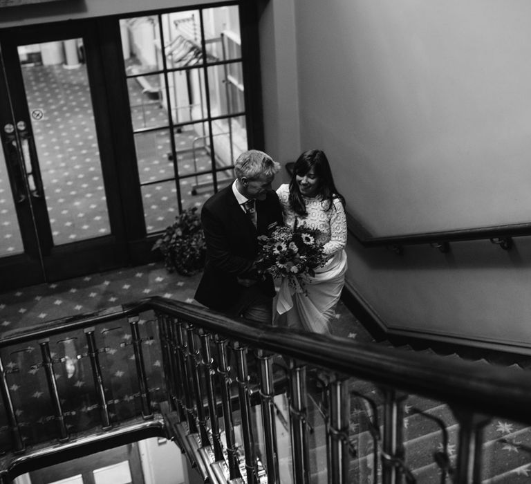 Bride in Self Portrait dress holding colourful bouquet walks up stairs with groom inside Bristol Registry Office